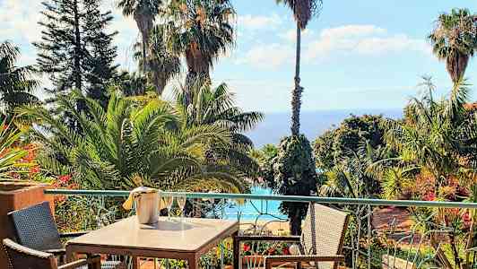 Spisebord på en terrasse med udsigt over tropiske træer, en pool og havet. (AI-genereret tekst)