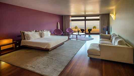 Moderne indrettet hotelværelse med en dobbeltseng, sofa, siddegruppe og store vinduer med udsigt. (AI-genereret tekst)