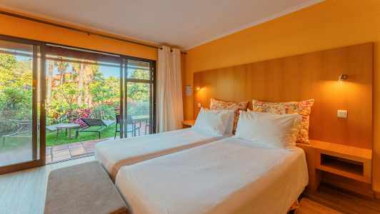 Et hotelværelse med to enkeltsenge, bløde puder og et stort glasvindue med udsigt til en have. (AI-genereret tekst)