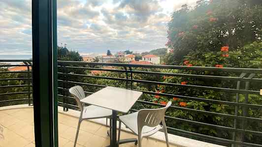 En altan med et bord og to stole, udsigt over hustage og træer. (AI-genereret tekst)