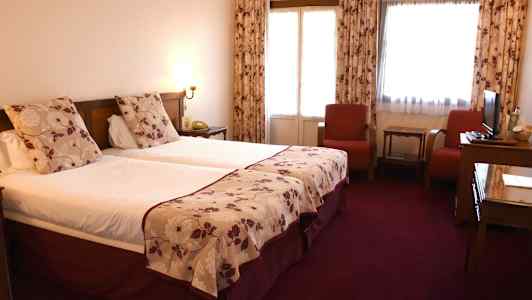 Dobbeltværelse med to enkeltsenge, røde stole og et bord. (AI-genereret tekst)