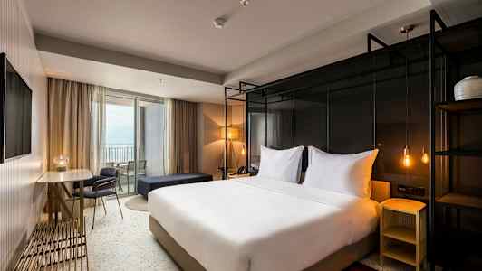 Hotelværelse med en dobbeltseng, bord og stole samt en balkon. (AI-genereret tekst)