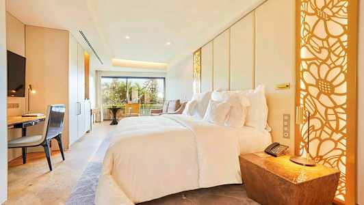 Et moderne hotelværelse med en stor seng, skrivebord, stol og altan med udsigt. (AI-genereret tekst)