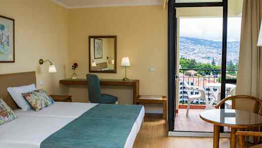 Hotelværelse med dobbeltseng, skrivebord og altan med udsigt. (AI-genereret tekst)