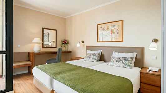 Billede af et hotelværelse med to enkeltsenge med hvidt sengetøj og grønne tæpper, et skrivebord med spejl og en stol i baggrunden. (AI-genereret tekst)