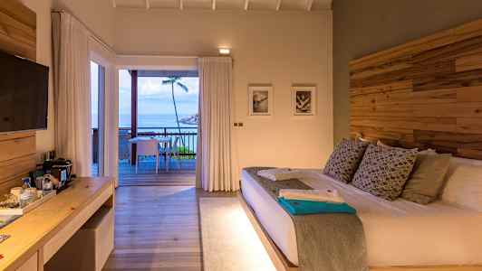 Et hotelværelse med en stor seng og adgang til en terrasse med udsigt over havet. (AI-genereret tekst)