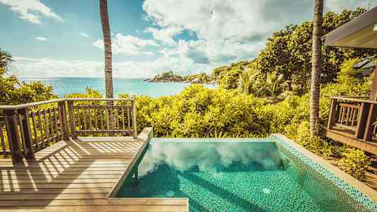 Udsigt fra en træterrasse og en pool over en tropisk have og havet. (AI-genereret tekst)