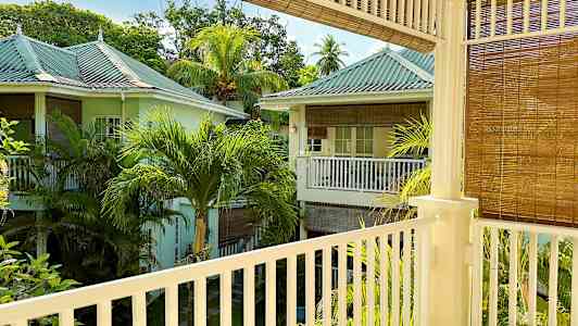 En udsigt fra en altan, der viser et frodigt område med pastelfarvede huse og palmer. (AI-genereret tekst)