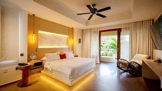 Et moderne soveværelse med en stor seng, siddepladser og en åben balkon med udsigt over grønt. (AI-genereret tekst)