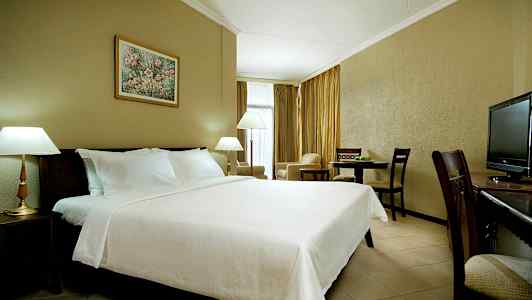 Et hotelværelse med en stor redt seng, lamper, spisebord og et fjernsyn. (AI-genereret tekst)