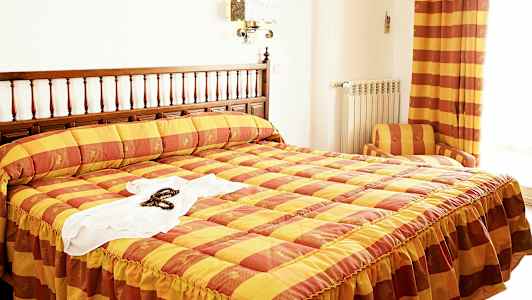 Et hotelværelse med en seng med et gul og orange ternet sengetæppe. (AI-genereret tekst)