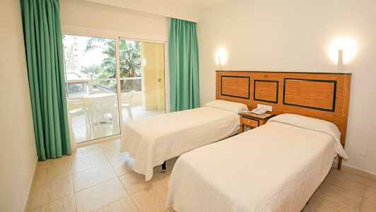 Hotelværelse med to enkeltsenge, en lille terrasse med møbler og udsigt til palmer. (AI-genereret tekst)