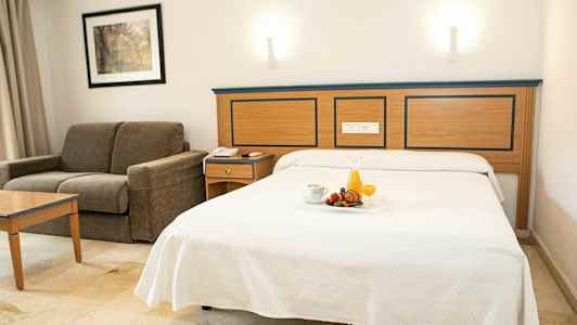 Hotelværelse med redt seng og sofa. (AI-genereret tekst)