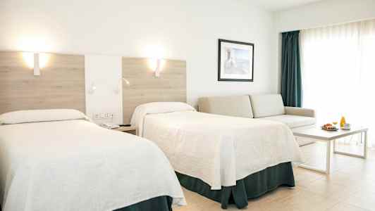 Et hotelværelse med to senge, en sofa, et bord og en morgenmadsservering. (AI-genereret tekst)