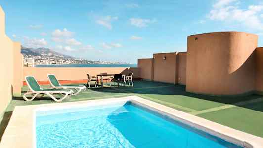 En terrasse med pool, liggestole og udsigt over havet. (AI-genereret tekst)