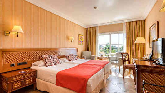 Billede af et hotelværelse med to senge, stol og bord, samt en TV. (AI-genereret tekst)