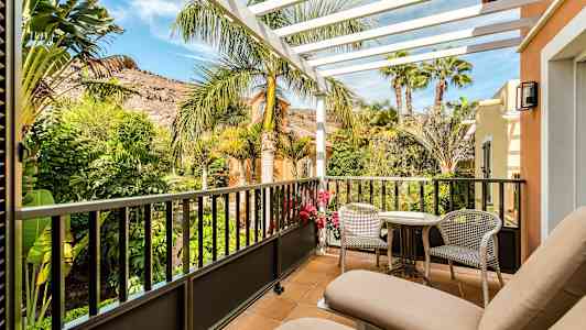 En altan med to liggestole, bord og stole. Udsigt til frodig have og bjerge. (AI-genereret tekst)