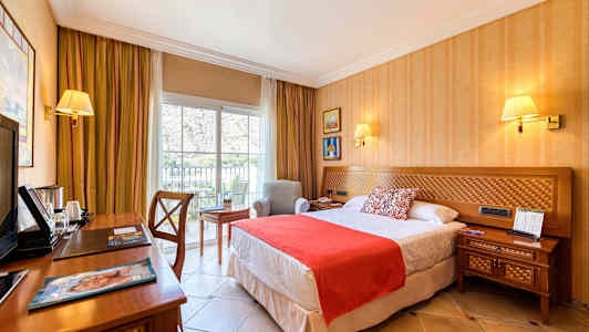 Et hotelværelse med en seng, natbord, skrivebord og en lænestol ved et vindue. (AI-genereret tekst)