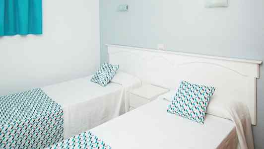 To enkeltsenge med hvidt sengetøj og mønstrede puder og sengetæpper. (AI-genereret tekst)