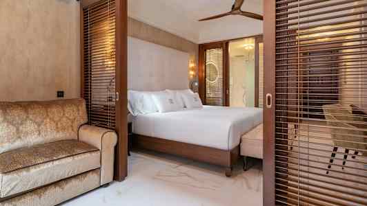 Et hotelværelse med en dobbeltseng og en sofa, afskærmet med træpersienner. (AI-genereret tekst)