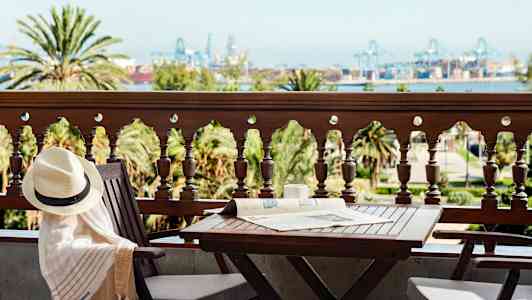 En altan med bord og stole, udsigt over træer og industriområde i det fjerne. (AI-genereret tekst)