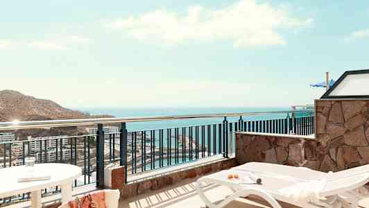 Udsigt fra en terrasse med liggestole og hav i baggrunden. (AI-genereret tekst)