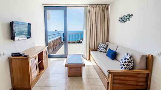 Et hotelværelse med siddeområde og udsigt til havet fra en balkon. (AI-genereret tekst)