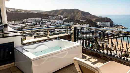 En terrasse med boblebad og udsigt over en bugt med hoteller og strand. (AI-genereret tekst)