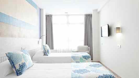 To enkeltsenge med blå og hvide sengesæt i et lyst værelse med et stort vindue. (AI-genereret tekst)