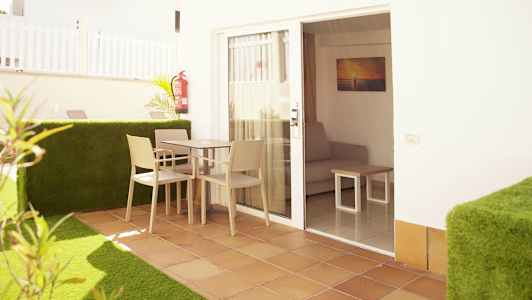 En terrasse med et bord og stole foran en dør, der fører ind til et rum med en sofa. (AI-genereret tekst)