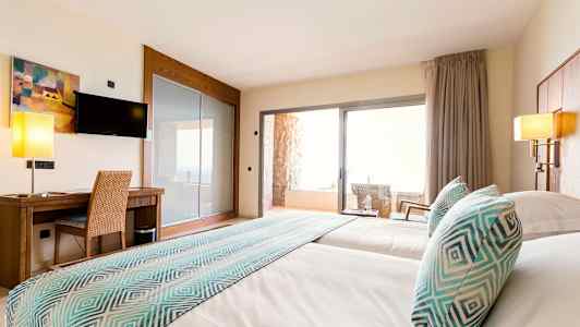 Billede af et hotelværelse med to senge, et skrivebord, et fjernsyn og en balkon med stole. (AI-genereret tekst)