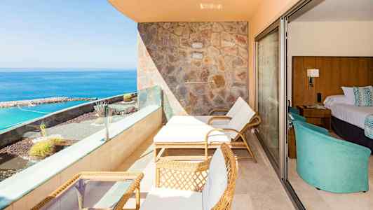 En terrasse med liggestole, bord og havudsigt, ved siden af et hotelværelse. (AI-genereret tekst)