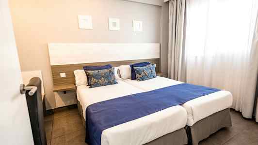 Hotelværelse med to enkeltsenge ved siden af hinanden, blå sengetæpper og dekorative puder. (AI-genereret tekst)