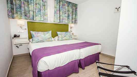 Soveværelse med en dobbeltseng, grøn sengegavl, lilla overkast og gardiner med mønster. (AI-genereret tekst)