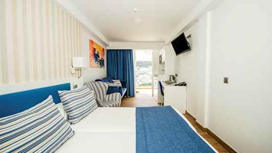 Et hotelværelse med en dobbeltseng med blåt sengetæppe og stribede puder. (AI-genereret tekst)