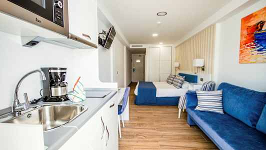 Et hotelværelse med en seng, blå sofa og tekøkken med vask. (AI-genereret tekst)