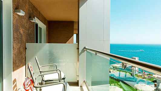 Altan med to stole, glasrækværk og udsigt over havet. (AI-genereret tekst)