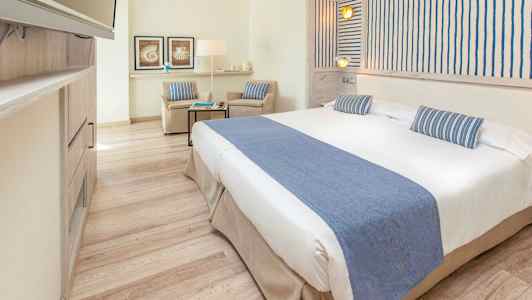 Et lyst hotelværelse med en bred seng og blå dekorationer. (AI-genereret tekst)