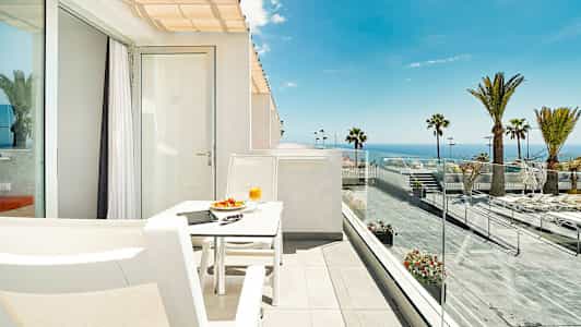 En solrig terrasse med udsigt over havet, udstyret med en hvid siddegruppe. (AI-genereret tekst)