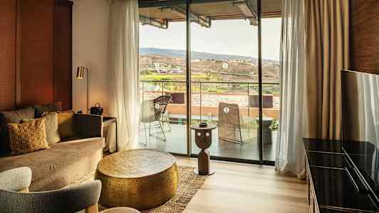 En indrettet hotelsuite med en siddegruppe og udsigt til en balkon og landskab. (AI-genereret tekst)