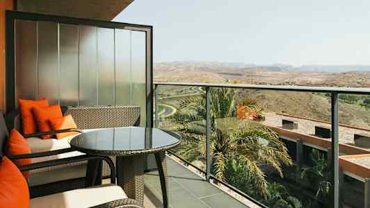 Altan med siddepladser, glasbord og udsigt over omgivelser med palmer og landskab. (AI-genereret tekst)