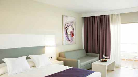 Hotelværelse med seng, sofa, sofabord og gardiner. (AI-genereret tekst)