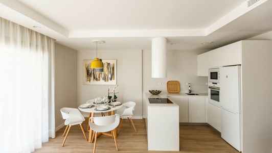 Moderne køkken med spiseområde, hvide møbler og lys indretning. (AI-genereret tekst)