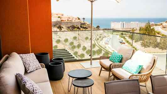 Terrasse med siddepladser under en parasol og udsigt over havet. (AI-genereret tekst)