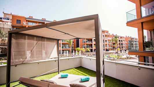 En moderne solseng med parasol på en græsplæne, omgivet af beboelsesbygninger og en pool. (AI-genereret tekst)