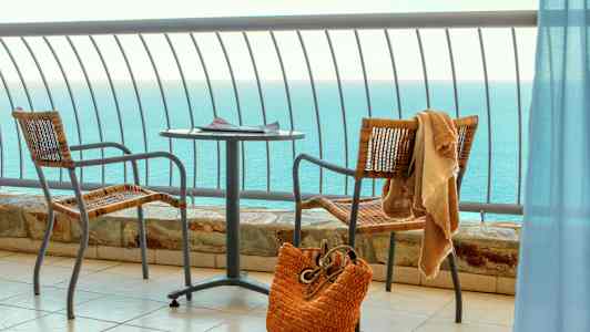 Udsigt over havet fra en altan med bord, to stole og en strandtaske. (AI-genereret tekst)