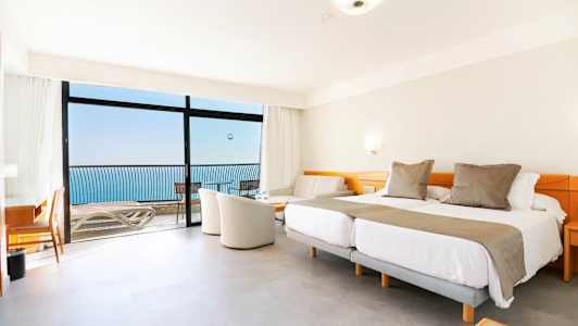 Et hotelværelse med dobbeltsenge, siddeområde og altan med havudsigt. (AI-genereret tekst)