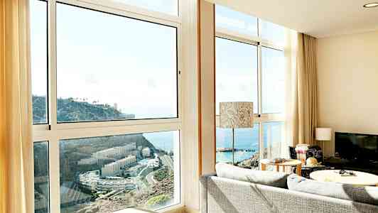 Stue med store vinduer, der viser udsigt over havet og en klippe. (AI-genereret tekst)