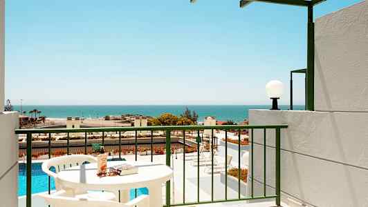 En altan med udsigt over en pool og havet, bord og stole synlige. (AI-genereret tekst)