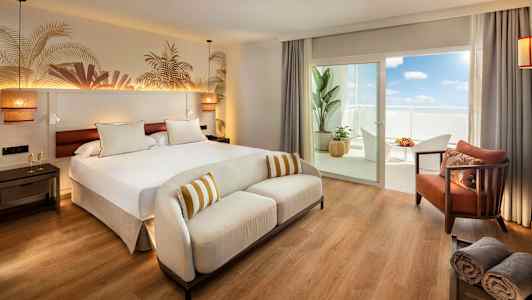 Et hotelværelse med en stor seng, en hvid sofa og en balkon med møbler. (AI-genereret tekst)